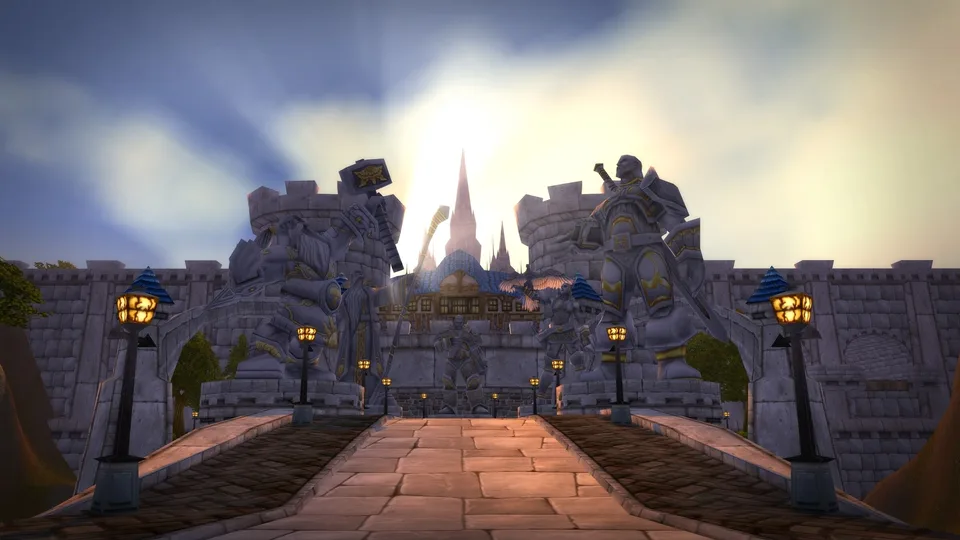 The Gate of Stormwind City seen from the bridge approach at sunrise, with the stone statues and cathedral spire behind.